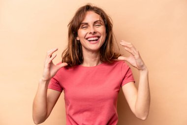 Beyaz tenli genç bir kadın bej arka planda izole edilmiş. Elinde avuç içi olan bir şeyle kameraya sunuyor..