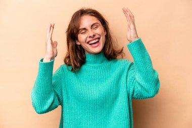 Beyaz tenli genç bir kadın, bej arka planda izole edilmiş neşeli bir şekilde gülüyor. Mutluluk kavramı.