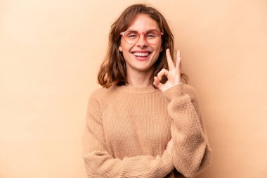 Beyaz tenli genç bir kadın bej arka planda izole edilmiş bir şekilde göz açıp kapayıncaya kadar iyi bir jest yapıyor..