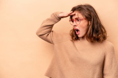 Beyazlı genç bir kadın bej arka planda izole edilmiş, uzaklara bakıyor ve elini alnına koyuyor..