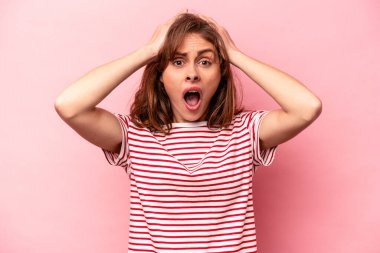 Pembe arka planda izole edilmiş genç beyaz kadın şaşırmış ve şok olmuş..