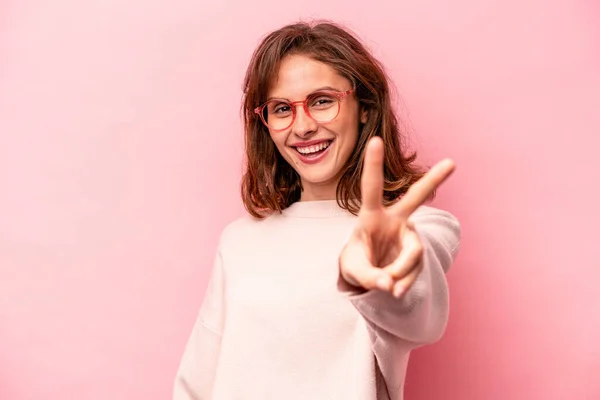 ピンクの背景に孤立した若い白人女性喜びと屈託のない指で平和のシンボルを示す — ストック写真