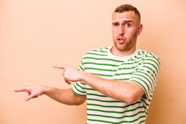 Beyazların arka planında izole edilmiş genç beyaz adam işaret parmağıyla fotokopi alanını işaret ederek şok oldu..