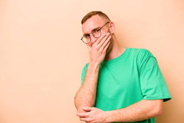 Beyaz tenli genç adam bej arka planda izole edilmiş gülerek, kaygısız, doğal duygularla gülüyor..