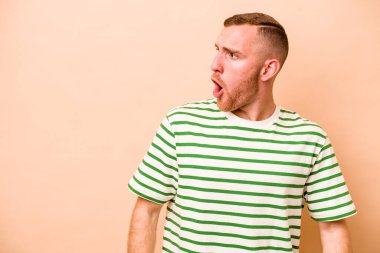 Beyazlı genç bir adam bej arka planda izole edilmiş. Gördüğü bir şey yüzünden şok oluyor..