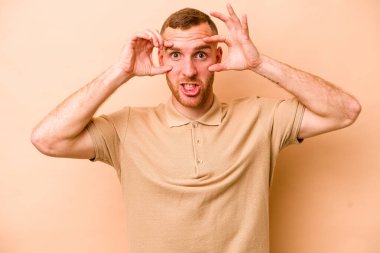 Beyazlı genç bir adam bej arka planda izole edilmiş. Başarı fırsatı bulmak için gözlerini açık tutuyor..