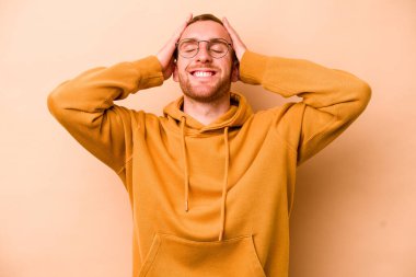 Beyazlı genç bir adam bej arka planda izole edilmiş, mutlu bir şekilde ellerini başının üstünde tutarak gülüyor. Mutluluk kavramı.