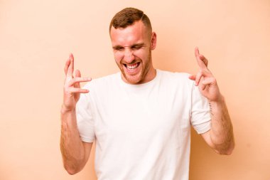 Beyazlı genç adam bej arka planda izole edilmiş şans dilemek için şans diliyor.