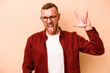 Beyaz tenli genç adam bej arka planda izole edilmiş. Parmaklarıyla kaya hareketi gösteriyor.