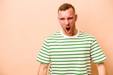 Beyazlı genç bir adam bej arka planda izole edilmiş çok kızgın, öfkeli, hayal kırıklığına uğramış.