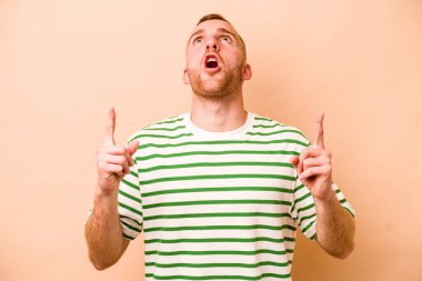 Beyazlı genç bir adam bej arka planda izole edilmiş. Ağzı açık, üst tarafı işaret ediyor..