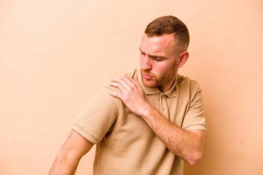 Beyaz tenli genç adam bej arka planda izole edilmiş, omuz ağrısı var..