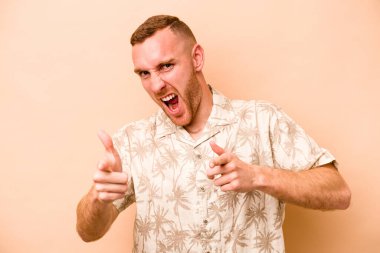 Beyaz tenli genç adam bej arka planda izole edilmiş. Önü işaret eden neşeli gülümsemeler..