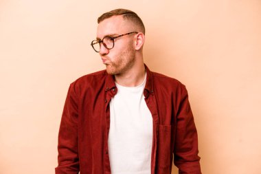 Beyazlı genç adam bej arka planda izole edilmiş omuzlarını silkeliyor ve gözleri açık..