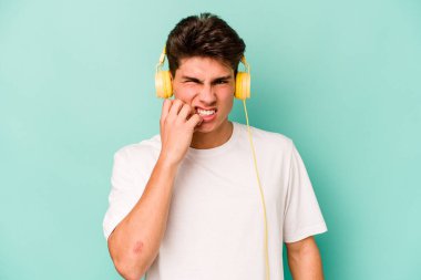 Mavi arka planda müzik dinleyen, tırnak yiyen, gergin ve endişeli genç beyaz bir adam..
