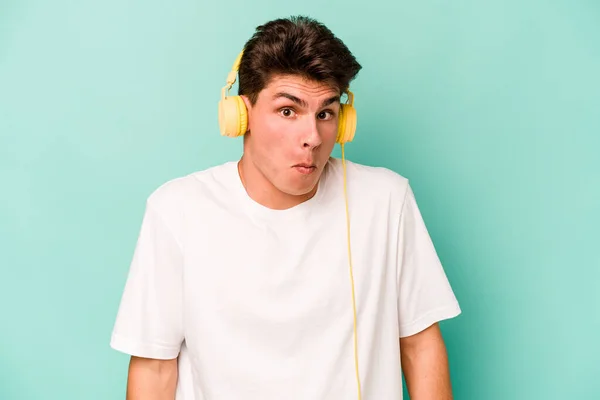 Mladý Běloch Naslouchá Hudbě Izolované Modrém Pozadí Pokrčí Rameny Otevřené — Stock fotografie