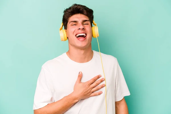 Joven Hombre Caucásico Escuchando Música Aislada Sobre Fondo Azul Ríe — Foto de Stock