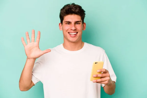 Młody Biały Mężczyzna Trzyma Telefon Komórkowy Odizolowany Niebieskim Tle Uśmiechnięty — Zdjęcie stockowe
