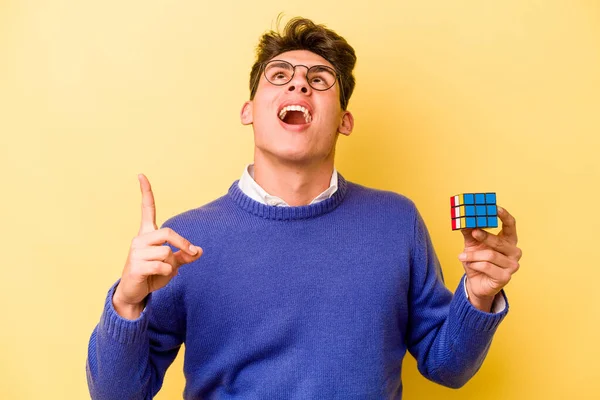 Mladý Běloch Drží Rubiks Kostku Izolované Žlutém Pozadí Ukazuje Vzhůru — Stock fotografie