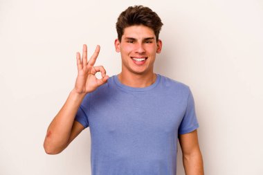 Beyaz arka planda izole edilmiş genç beyaz bir adam bir göz kırptı ve elleriyle iyi bir jest yaptı..