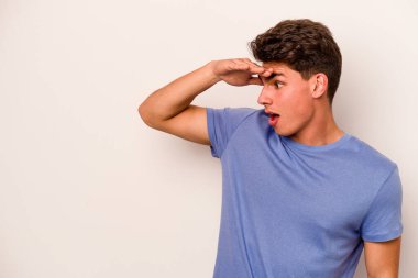 Beyaz arka planda izole edilmiş genç beyaz bir adam uzaklara bakıyor ve elini alnına koyuyor..