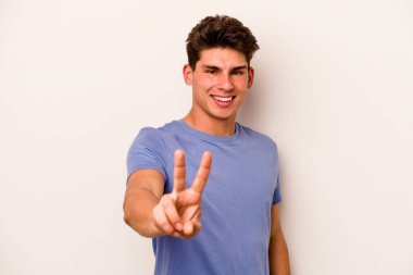 Beyaz arka planda izole edilmiş genç beyaz bir adam zafer işareti gösteriyor ve gülümsüyor..