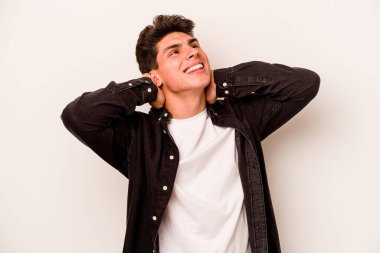 Beyaz arka planda izole olmuş genç beyaz bir adam kendini güvende hissediyor, elleri başının arkasında..