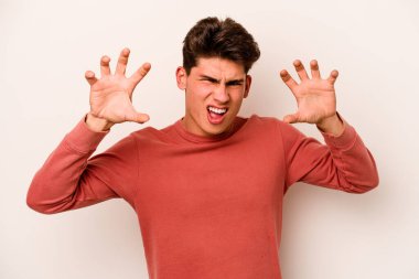 Beyaz arka planda izole edilmiş genç beyaz bir adam pençelerini kedi taklidi yaparken gösteriyor, agresif bir hareket..