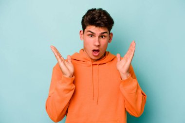 Kafkasyalı genç adam mavi arka planda izole edildi. Şaşırdı ve şok oldu..