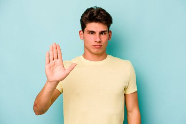 Mavi arka planda izole edilmiş genç beyaz adam gülümseyerek beş numarayı parmaklarıyla gösteriyor..