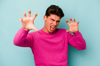 Mavi arka planda izole edilmiş genç beyaz adam gergin elleriyle çığlık atıyor..