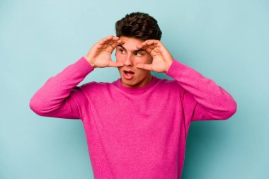 Mavi arka planda izole edilmiş genç beyaz adam bir başarı fırsatı bulmak için gözlerini açık tutuyor..