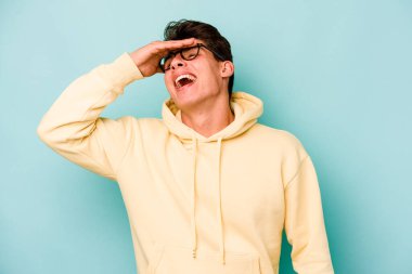 Mavi arka planda izole edilmiş genç beyaz adam ellerini başının üstünde tutarak neşe içinde gülüyor. Mutluluk kavramı.