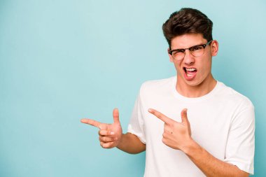 Mavi arka planda izole edilmiş genç beyaz adam işaret parmağıyla fotokopi alanını işaret ederek heyecan ve arzusunu ifade ediyor..