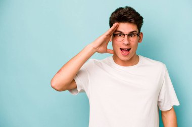 Mavi arka planda izole edilmiş genç beyaz adam yüksek sesle bağırıyor, gözleri açık ve elleri gergin tutuyor..