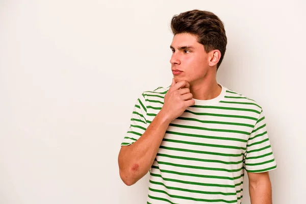 Young caucasian man isolated on white background looking sideways with doubtful and skeptical expression.