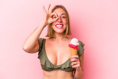 Genç beyaz kadın bikini giyiyor ve elinde pembe arka planda izole edilmiş bir dondurma tutuyor..