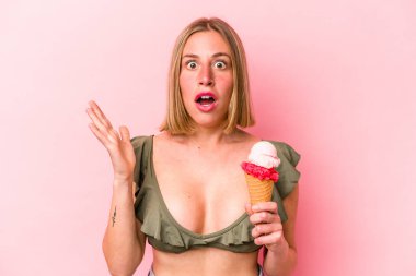 Genç beyaz kadın bikini giyiyor ve elinde pembe arka planda izole edilmiş dondurma tutuyor. Şaşırmış ve şok olmuş..