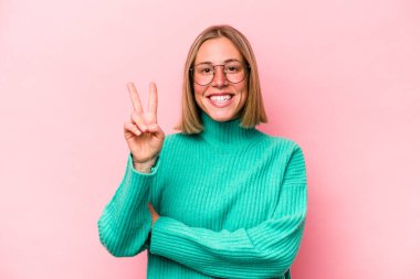 Pembe arka planda izole edilmiş genç beyaz kadın iki numarayı parmaklarıyla gösteriyor..