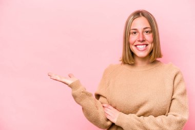 Pembe arka planda izole edilmiş genç beyaz kadın bir avuç içinde fotokopi alanı ve belinde bir el daha gösteriyor..
