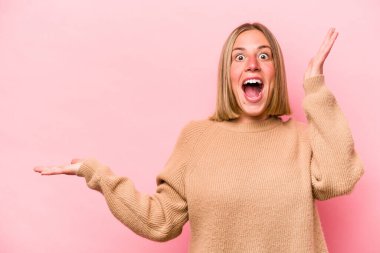 Pembe arka planda izole edilmiş genç beyaz kadın avuç içinde fotokopi alanı tutuyor, el üstünde tutuyor. Şaşırmış ve mutlu..