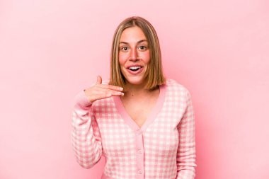 Pembe arka planda izole edilmiş genç beyaz kadın bir şeye gülüyor, elleriyle ağzını kapatıyor..