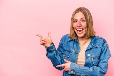 Pembe arka planda izole edilmiş genç beyaz kadın işaret parmaklarıyla işaret ederek heyecanlanıyor..