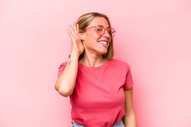 Pembe arka planda izole edilmiş genç beyaz kadın bir dedikoduyu dinlemeye çalışıyor..