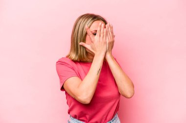 Pembe arka planda izole edilmiş genç beyaz kadın parmaklarıyla gözünü kırp korkmuş ve gergin..