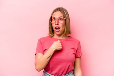 Pembe arka planda soyutlanmış beyaz bir kadın. Parmakla göstererek şaşırmış, geniş bir gülümsemeyle..