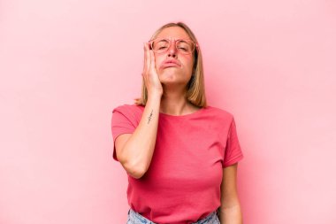 Pembe arka planda izole edilmiş genç beyaz kadın yorgun ve uykulu ellerini başının üstünde tutuyor..