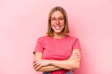 Pembe arka planda soyutlanmış genç beyaz kadın kendini güvende hissediyor, kararlılıkla kollarını kavuşturuyor..