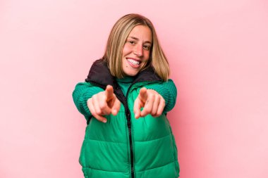 Pembe arka planda izole edilmiş genç beyaz kadın parmaklarıyla ön tarafı işaret ediyor..