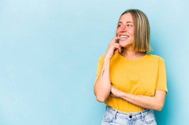 Mavi arka planda izole edilmiş genç beyaz kadın rahatça fotokopi odasına bakan bir şey düşünüyor..
